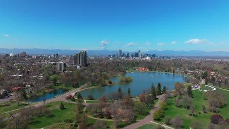 city park lodo denver colorado lake pavilion vibrant spring summer aerial drone sunny blue sky snow capped rocky mountains front range cityscape green lush grass trees blossom upwards motion