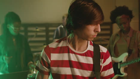 portrait of an energetic boy playing guitar during a band rehearsal in recording studio