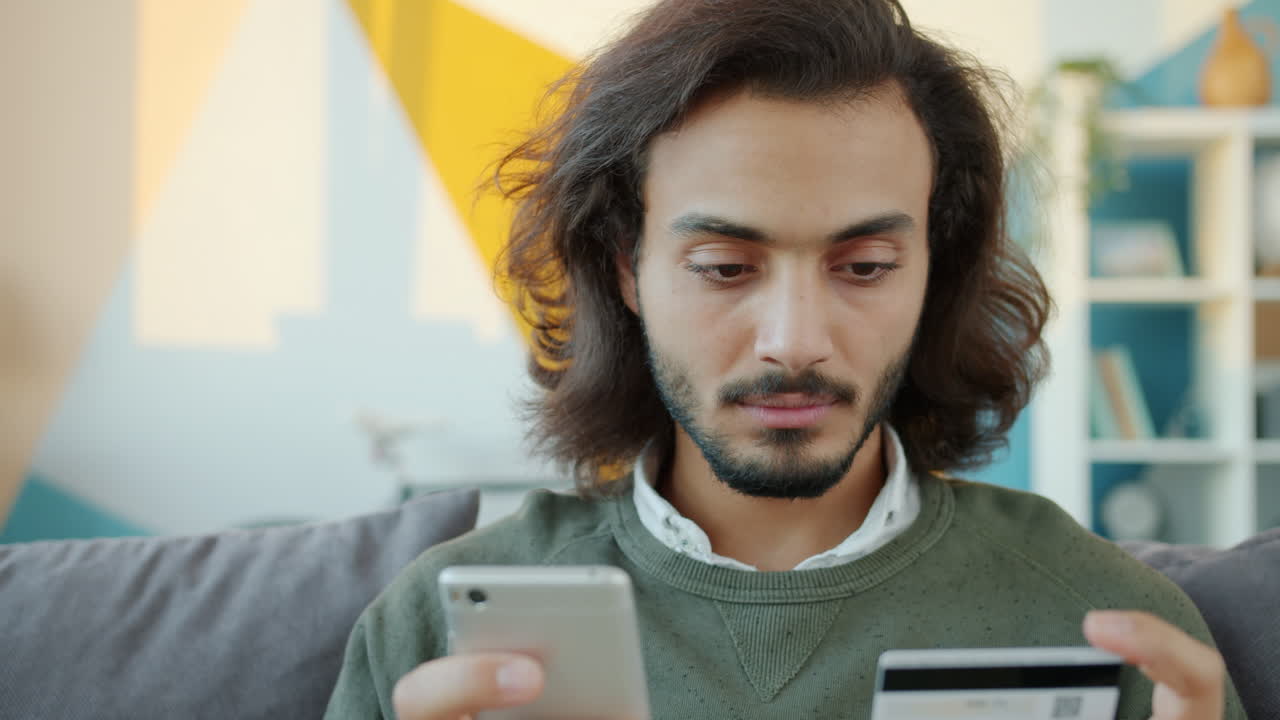 Man using mobile phone and credit card for online payment at home