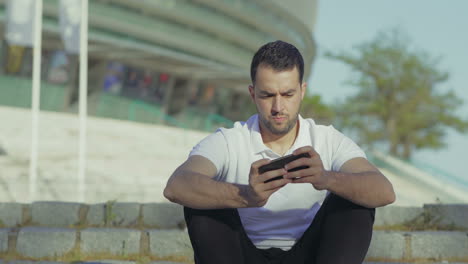 Excited-bearded-man-playing-video-game-on-smartphone-outdoor.