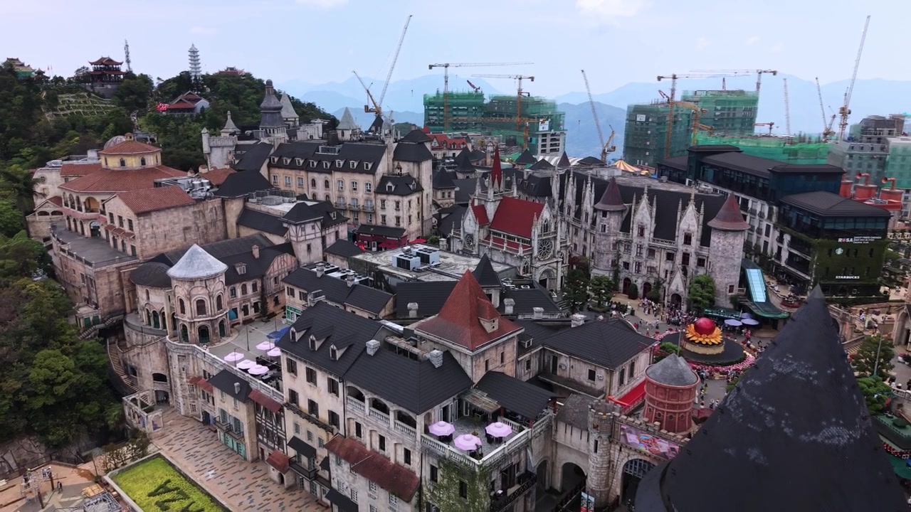 Bà Nà Hills SunWorld nổi bật với một quần thể các tòa nhà và điểm tham quan phong cách châu Âu nhìn từ trên cao, với núi non ở hậu cảnh dưới bầu trời ban ngày trong xanh.