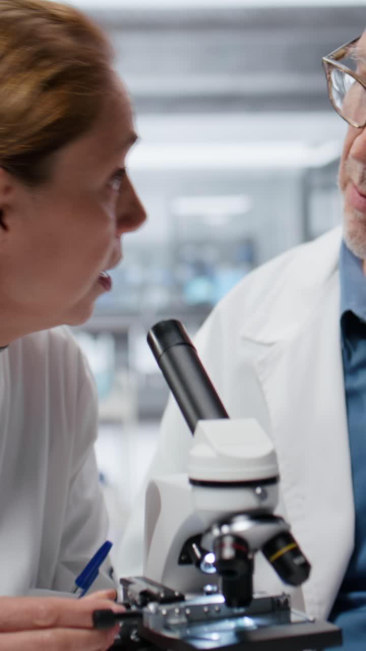 Video verticale di uno scienziato anziano che fa da mentore a una giovane donna nell’analisi di un vetrino di coltura batterica