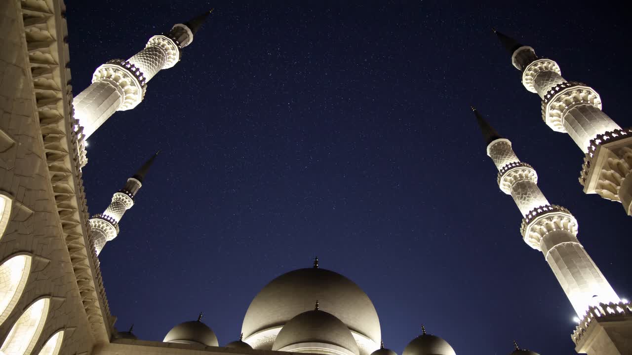 Video con angolazione dal basso di minareti illuminati di una moschea su un cielo notturno stellato