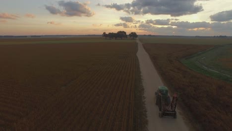 farmer driving large industrial commercial farm equipment along dirt road at sunrise