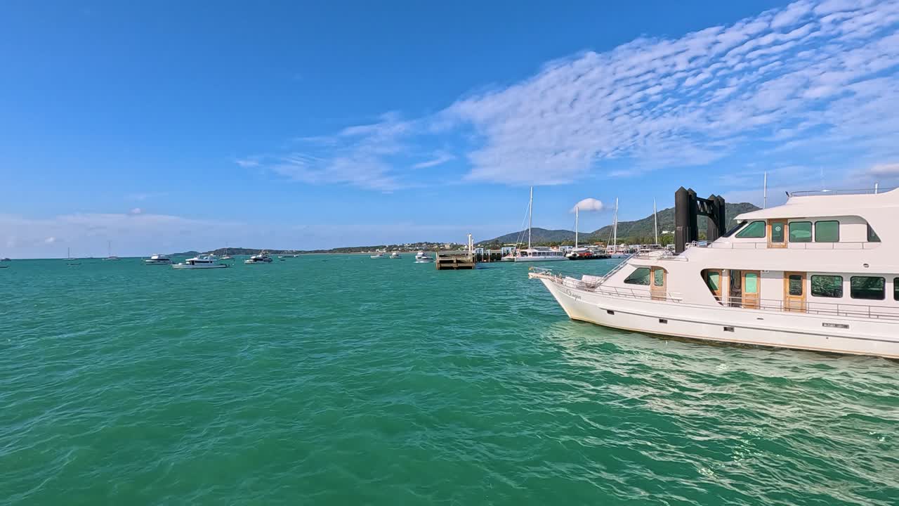 A motor yacht glides through Phuket's vibrant waters under clear skies, capturing the tranquil beauty of the sea and surrounding islands