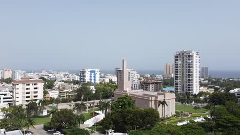 drone flight approaching the mormon temple in santo domingo, la esperilla area, aerial view of the city on sunny day