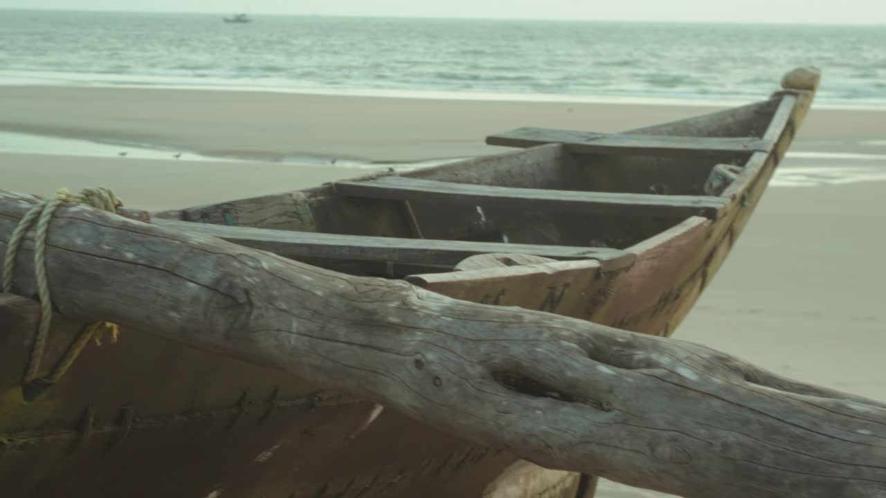Close-up tracking shot of a wooden boat resting on sand with the sea in the background