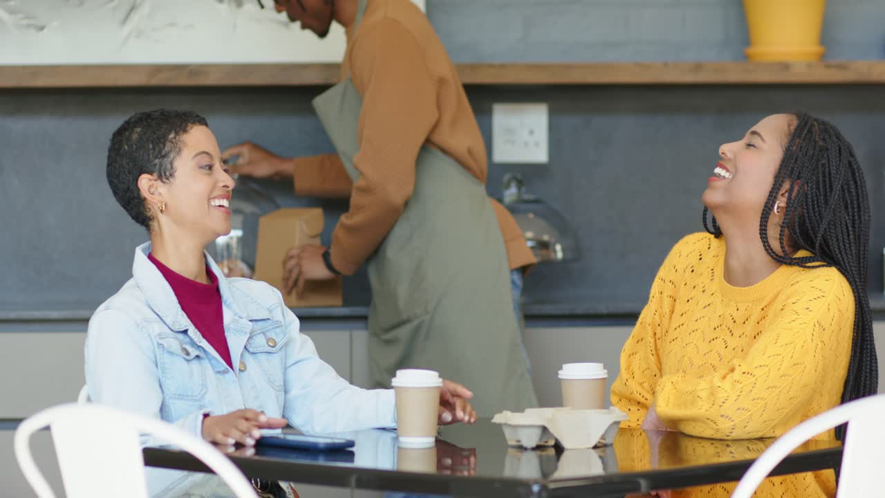Barista hebt eine Glaskuppel an und trägt eine Takeaway-Box aus Karton, während diverse Freundinnen lachen