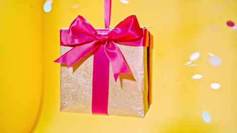 a festive gift box with pink ribbon on a yellow background