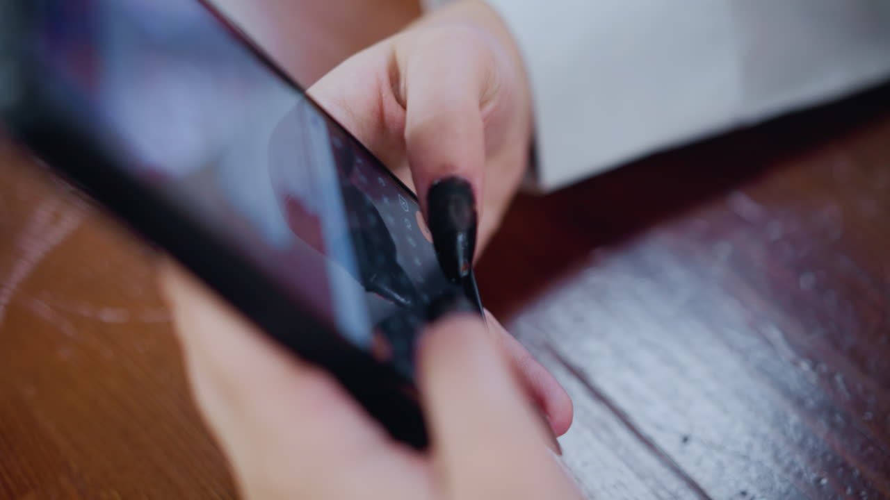 primer plano de un teléfono inteligente negro que se utiliza para escribir con las manos en una mesa de madera, mostrando la interacción en la pantalla, con enfoque en el teléfono y las uñas