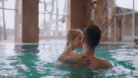 little girl and her father are playing in swimming pool of modern wellness center family weekend