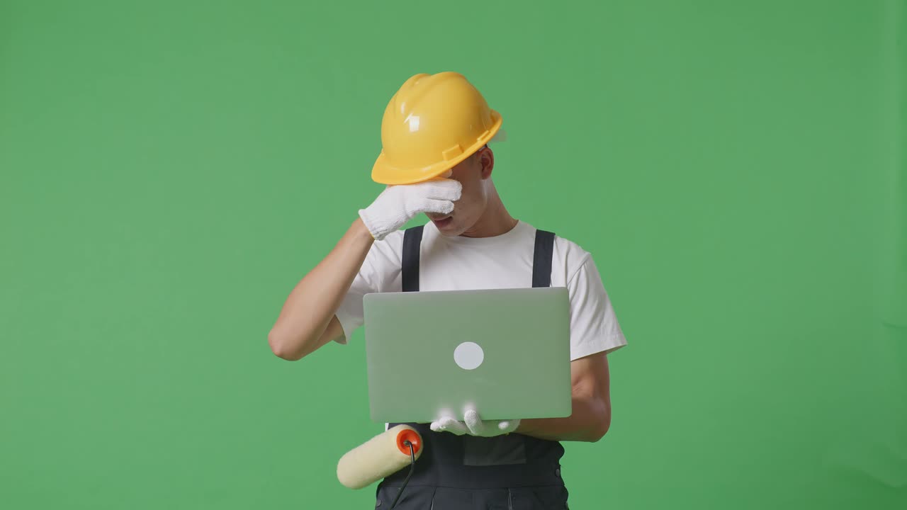 Asian Man Painter Wearing Safety Helmet Using A Laptop And Having A Headache While Standing In The Green Screen Background Studio