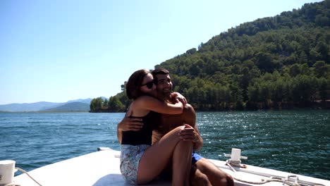 young pair sitting on bow of boat and posing to photographer at sunny day. happy couple in love spending time together on deck of ship and enjoying summer travel. concept of vacation or holiday. close up