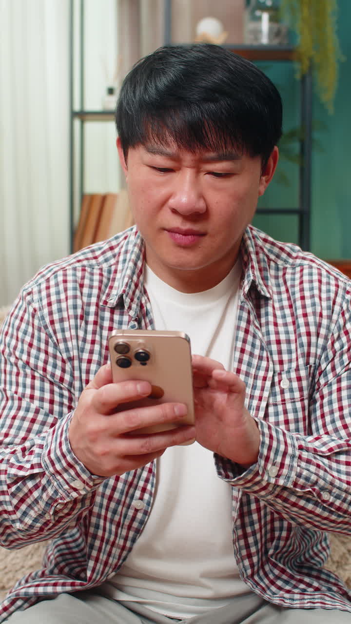 Asian man frowning at smartphone disappointed expression frustrated after reading bad news at home