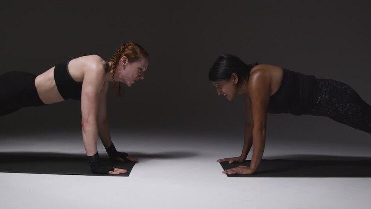 fotografía de estudio de dos mujeres maduras con ropa de gimnasia haciendo ejercicio de tabla juntas 2