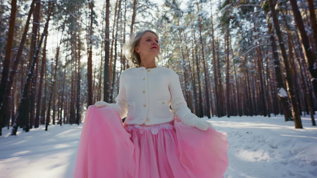 Donna elegante in gonna rosa in piedi in una foresta invernale innevata