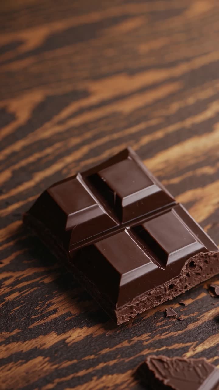 Close-up video of a dark chocolate bar on a wooden surface, shot from a top-down angle