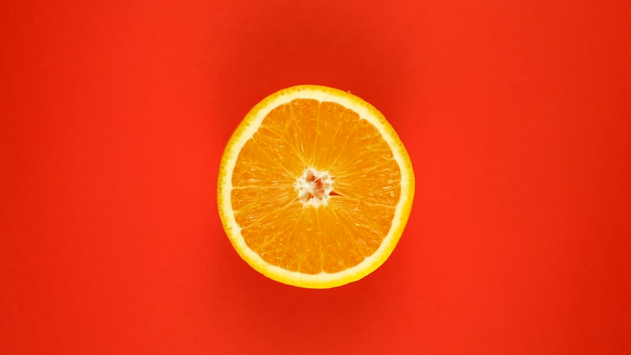 TOP VIEW: Half of an orange rotates on a red surface - Slow motion