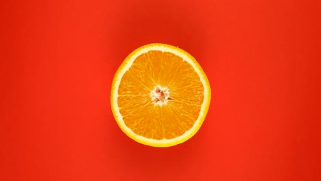 vista de arriba: la mitad de una naranja gira sobre una superficie roja - movimiento lento