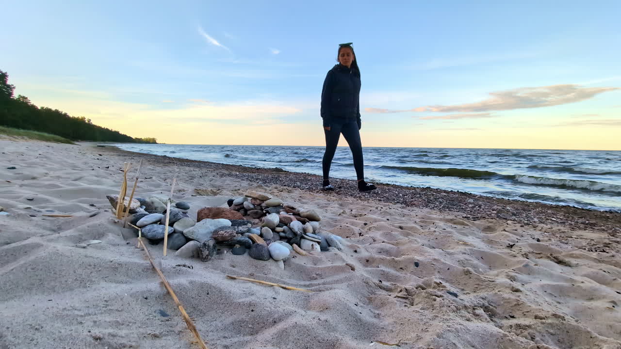 woman walks along the sandy Engure beach near a rock pile at sunset. Engure, Latvia