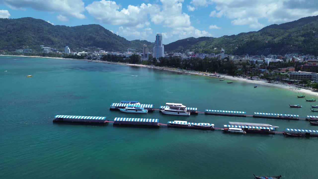 Quang cảnh trên không của Bãi biển Patong, cho thấy một cầu tàu nổi với những chiếc thuyền neo đậu dọc bờ biển nhiệt đới và làn nước xanh ngọc trong vắt ở Phuket Thái Lan, một điểm đến du lịch nổi tiếng