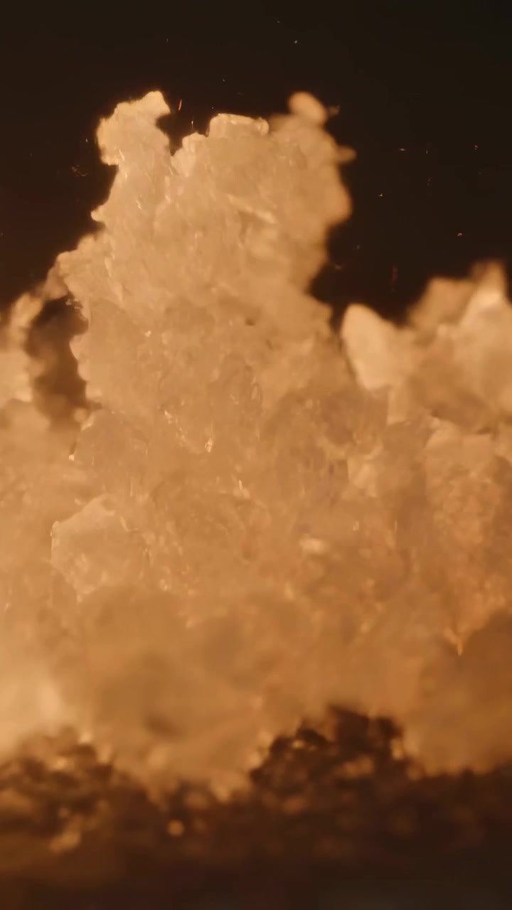 Video verticale: Cime di cristallo che si muovono lanciando scaglie in macro sopra un vassoio scuro, luce ambrata e polvere.
