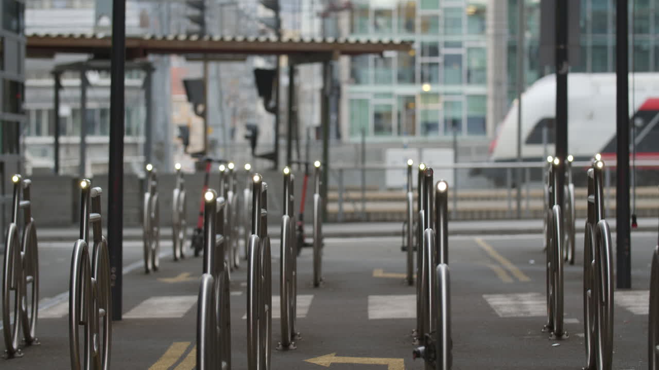 Cinematic medium wide 4K shot with slow parallax motion of illuminated steel bicycle parking stands and train leaving the central commerce train station, in Barcode Bjørvika Oslo Norway
