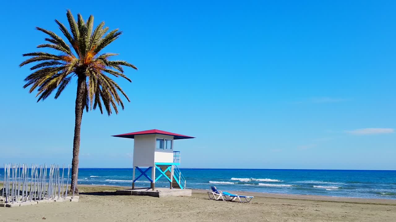 Lifeguard's cabin and a palm located on Mackenzie Beach. Waves of the Mediterranean sea on the background. Sunlight shot. Larnaca, Cyprus