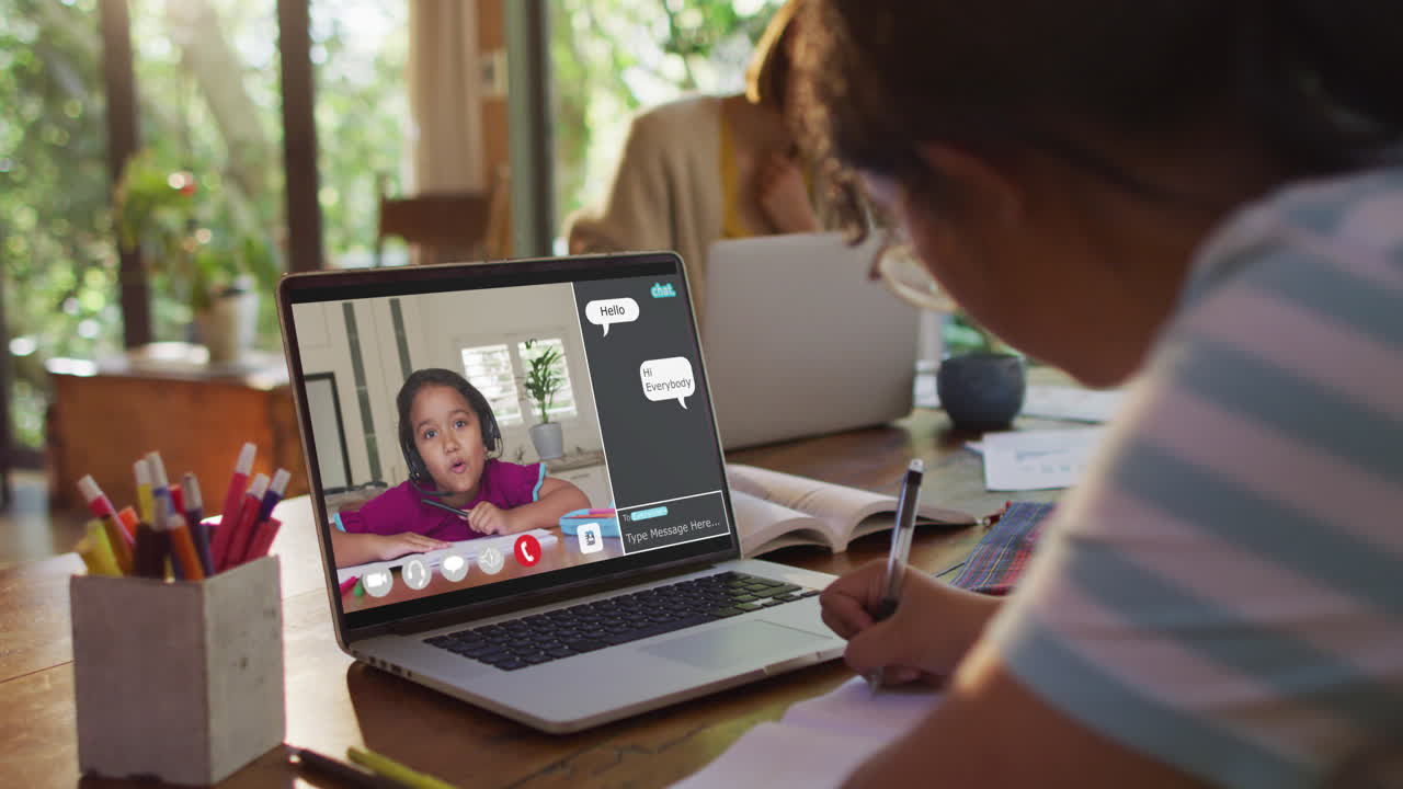 Schoolgirl using laptop for online lesson at home, with her colleague and web chat on screen