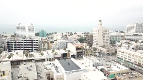 Panning-Aerial-View-of-Downtown-Santa-Monica,-California-with-Cars-and-People-walking-around-on-a-nice-day-with-the-Beach-and-Pacific-Ocean-in-the-Background