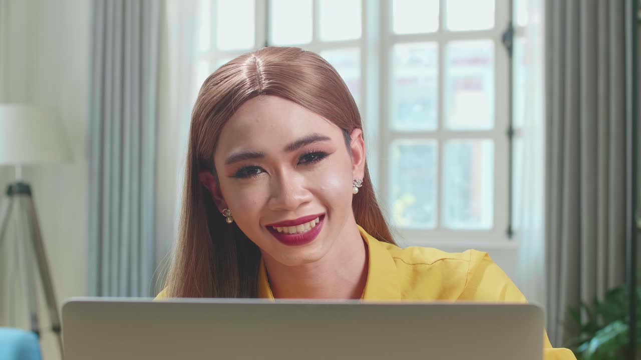 Asian Young Transgender Woman Working With Laptop Computer And Smiling To Camera In Living Room