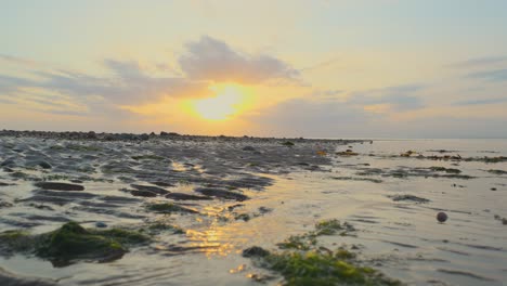 Low-angle-moving-water-on-shoreline-with-slow-pan-during-sunset-in-slow-motion-at-Fleetwood,-Lancashire,-UK