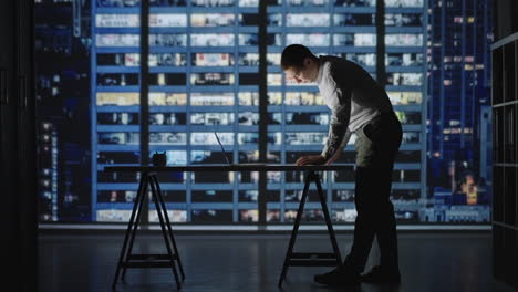 confident manager working late night in office. man standing in office lean over desk working on laptop. architects working on construction project