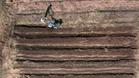 Aéreo---Hombre-Trabajando-En-Un-Campo-Con-Un-Motocultor,-Agricultura,-Tiro-Ancho-Inclinado-Hacia-Arriba