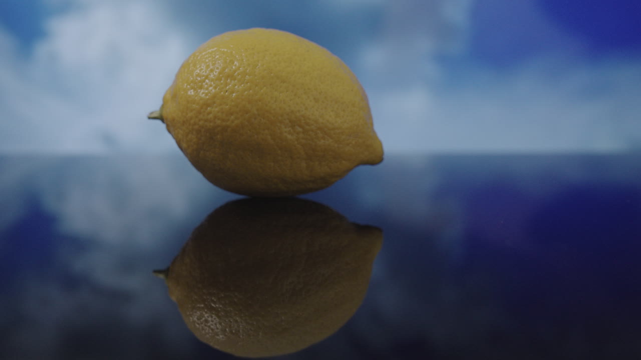 Time-lapse di un limone giallo appoggiato su una superficie asciutta riflettente, con nuvole che si muovono lentamente sullo sfondo durante una giornata nuvolosa