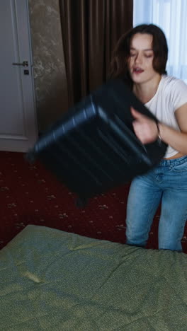 tired woman after packing suitcase. young woman puts packed luggage and falling down on bed in comfortable hotel room. the end of a trip. vertical video