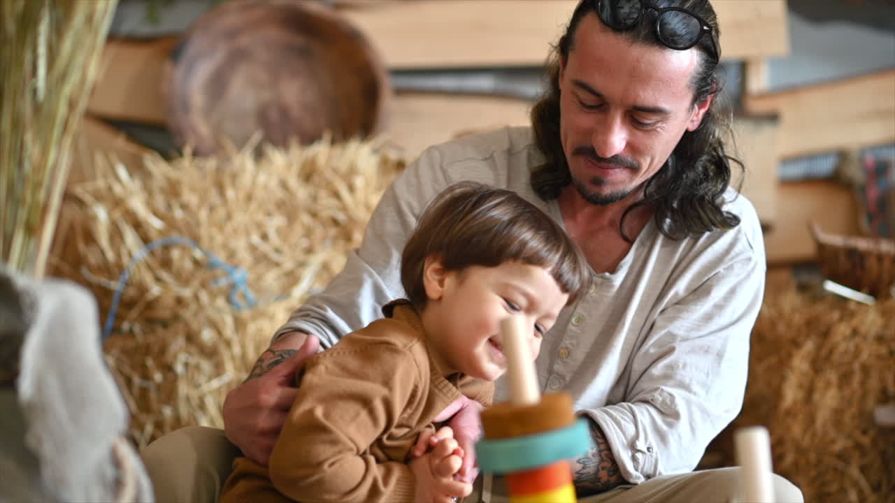 Father playing with his son in a barn, near square hay bales