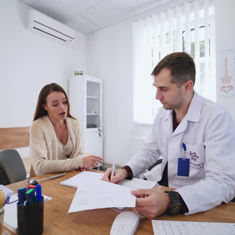 young woman is talking to a doctor in clinic. beautiful girl sitting in medical cabinet and having a conversation to a male specialist. healthcare concept.