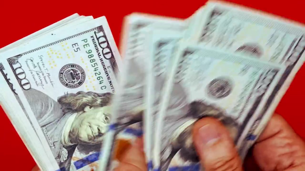 Primo piano delle mani di una persona che contano una mazzetta di banconote da cento dollari statunitensi (USD) su uno sfondo rosso semplice. Concetto di pagamento in contanti, ricchezza, transazione illegale, successo finanziario o pagamento dello stipendio