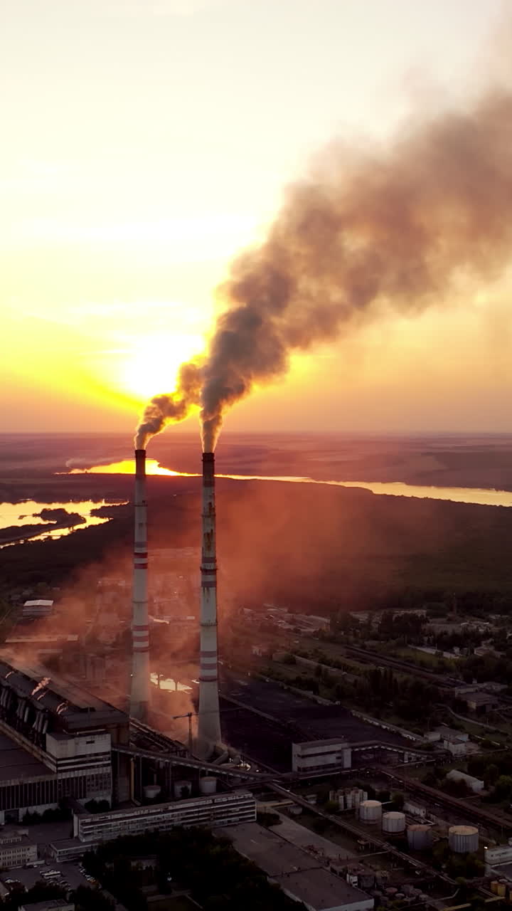 Aerial view on a huge industrial factory among nature. Dirty smoke coming into the air from factory pipes at sunset. Vertical video