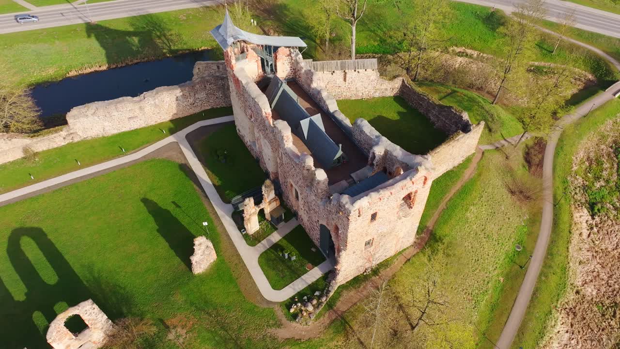 Ancient stone walls of Dobele Castle glow in warm sunlight and spring grass