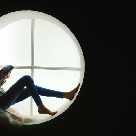 Woman-Reads-Magazine-Sitting-In-Round-Window