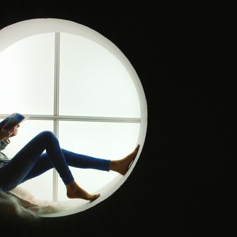 woman reads magazine sitting in round window