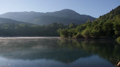 beautiful scenic countryside lake view of low fog, green forest and mountain in background, static