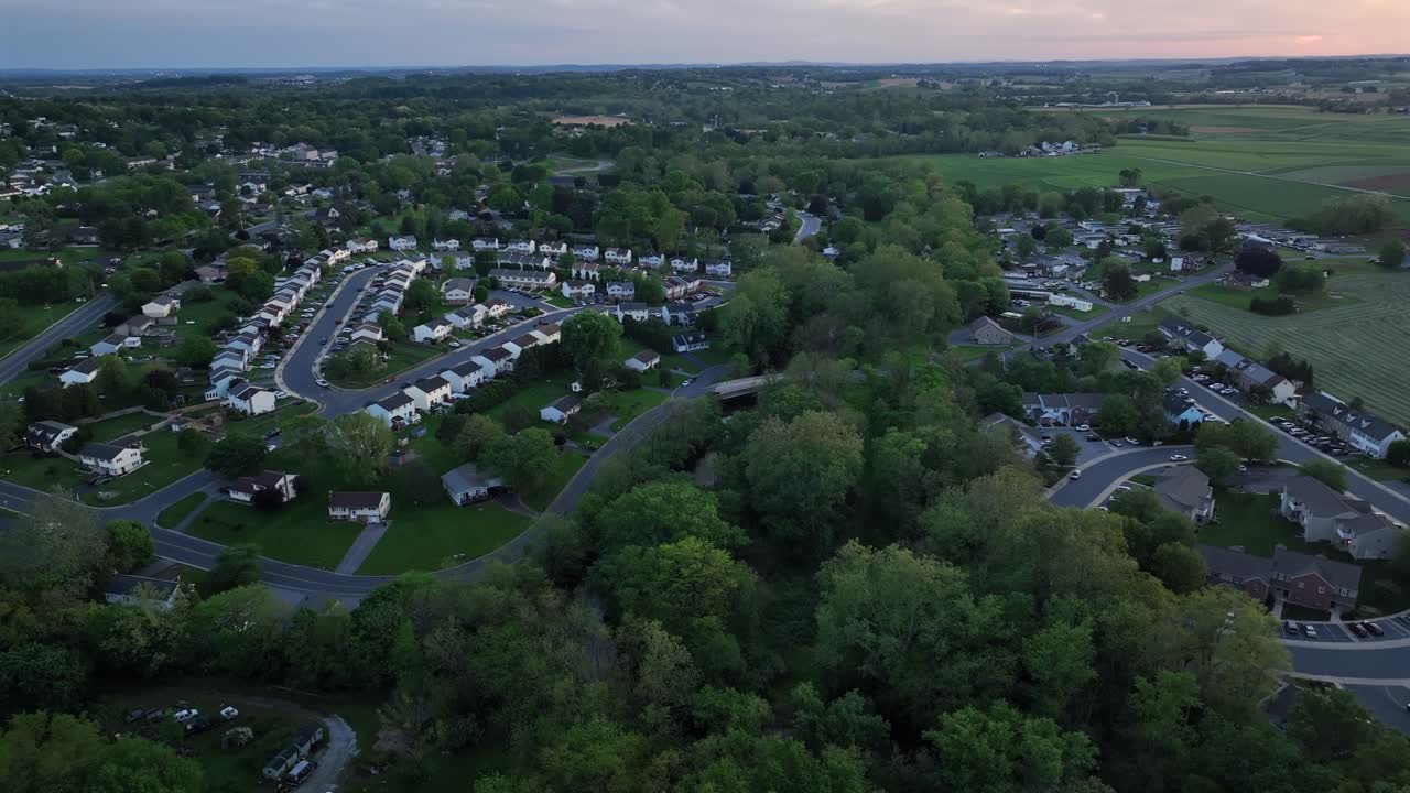 Row of modern houses and apartment buildings in suburb district of town. American city with green farm trees. Aerial approaching wide shot.
