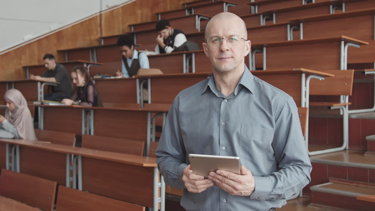 Professor with Tablet Posing for Camera in Lecture Hall with Students