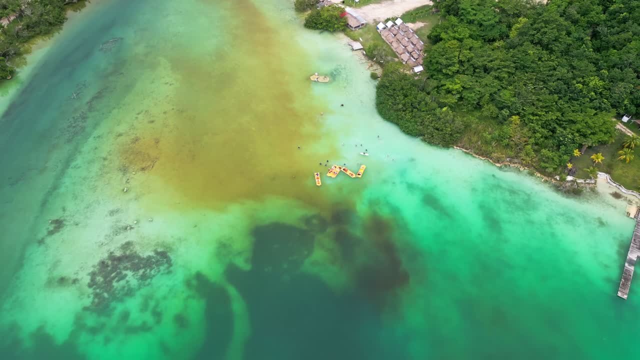 Aerial view of Bacalar, Mexico showing tourists, wooden floats and vibrant water near lush jungle in the Yucatán Peninsula. A lively lagoon escape with Caribbean charm