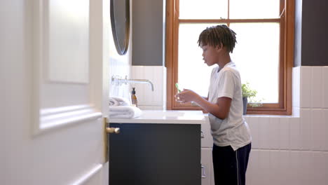 african american boy brushing teeth in bathroom at home, slow motion