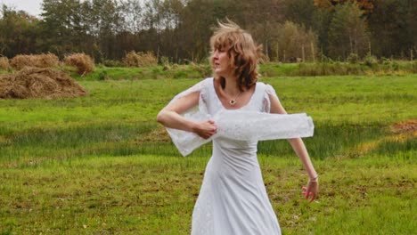 Woman-in-a-long-white-dress-dancing-in-a-green-meadow-in-ultra-slow-motion