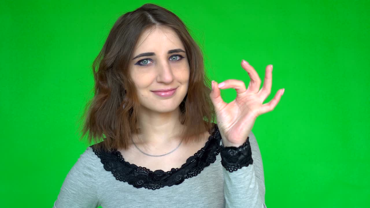 Happy young woman showing ok sign with fingers isolated on a green background.